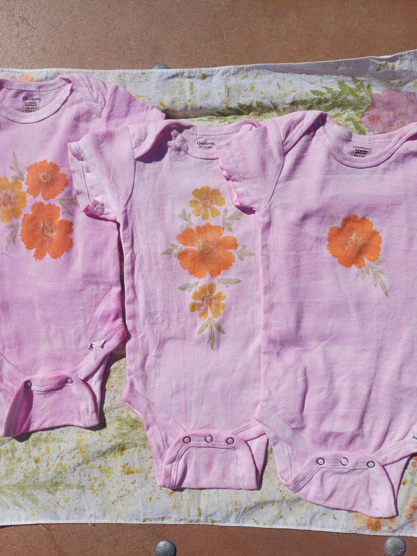 Three pink baby onesies with orange floral patterns