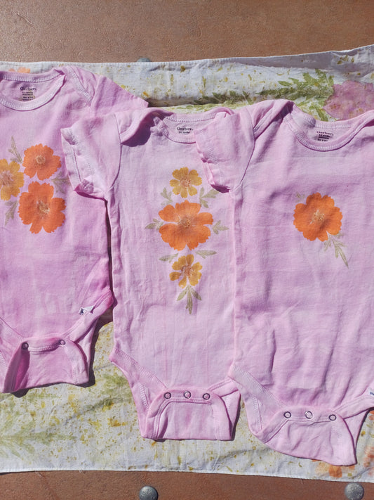 Three pink baby onesies with orange floral patterns