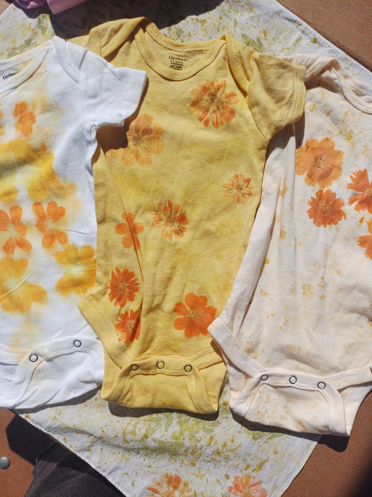 Three baby onesies with floral patterns on a floral blanket.